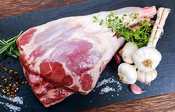 Raw lamb leg on blue stone background with herbs.